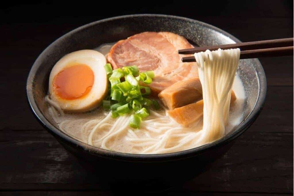 Tigela de ramen com macarrão amarelo elástico, caldo rico e toppings orientais, evidenciando textura perfeita e qualidade do macarrão Keishi no preparo profissional.