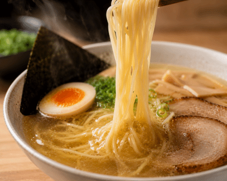 Shio ramen: o que é e qual macarrão combina melhor com esse caldo delicado 2 Macarrão fino sendo mergulhado em caldo claro de shio ramen, destacando transparência e leveza do prato.